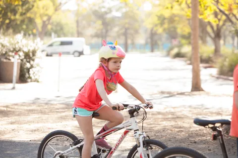A girl in a bright pink and orange top rides a small bike alone.