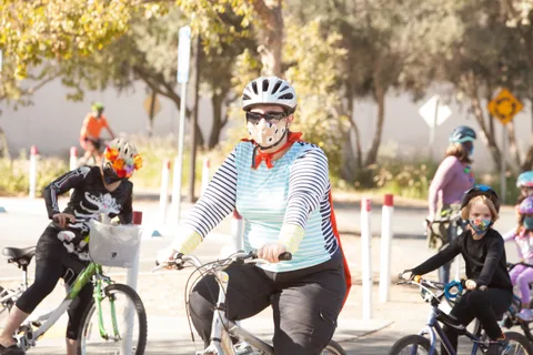 A woman in a striped shirt and red scarf with skeleton face makeup rides a bike.