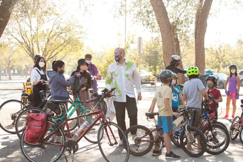 A group of kids and an adult gather with their bikes on the path.