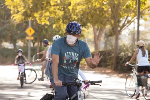 A masked rider in a Zombie Bike Parade t-shirt waves while other riders pass behind him.