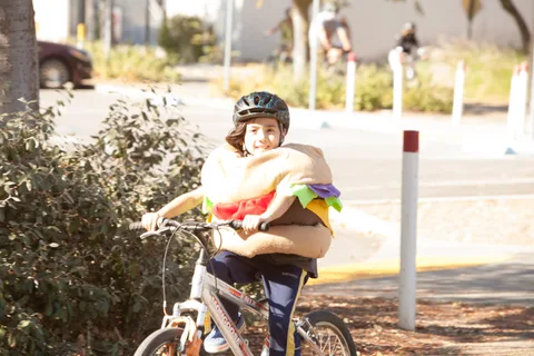 A kid in a soft taco costume rides a bike past.