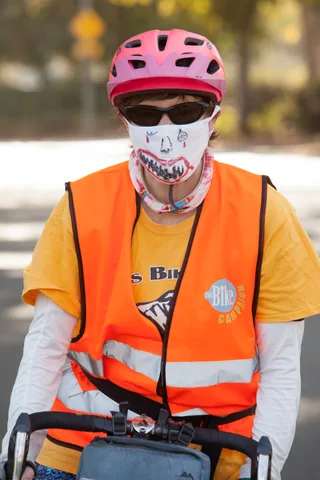 An event volunteer in an orange safety vest wears a mask painted like shark teeth.