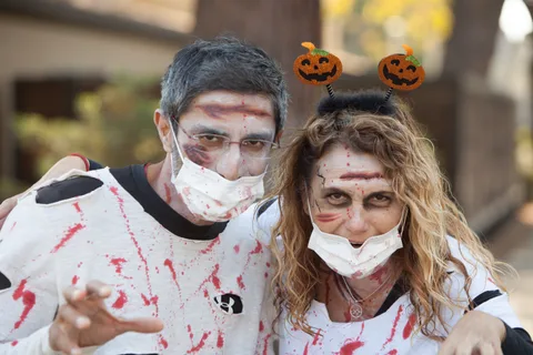A couple in blood-splattered zombie makeup and a pumpkin headband pose close together.