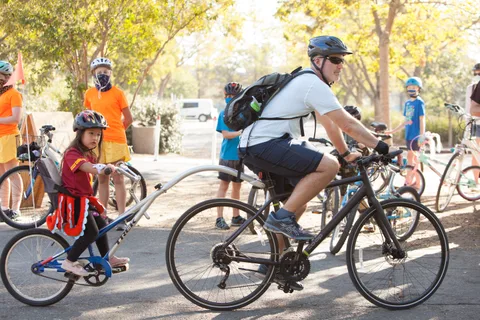 Riders pedal away from the camera along a tree-lined path.