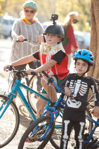 A child in a skeleton costume stands with a family and bikes.