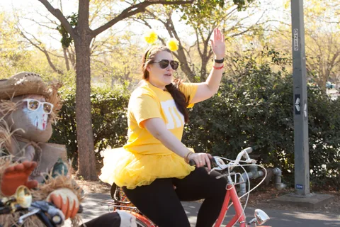 A woman in a yellow costume waves next to another rider in a straw-textured mask.