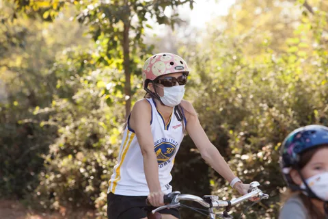 A masked rider in a basketball jersey pedals down the path.