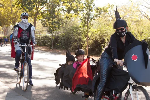 Riders in dark armored and caped costumes ride together on the path.