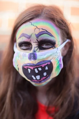 A woman with rainbow crackled face paint wears a matching painted mask.