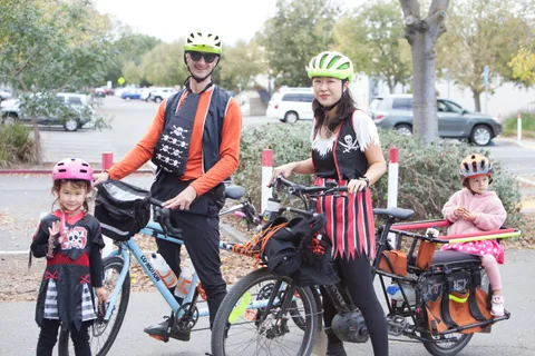 A family dressed as pirates poses with a cargo bike carrying two young children.
