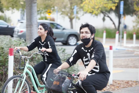 Two riders in matching skeleton shirts and masks pedal down the street.