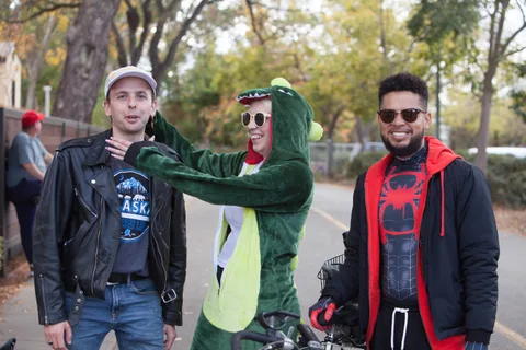 Three friends share a playful moment, one dressed as a dinosaur.
