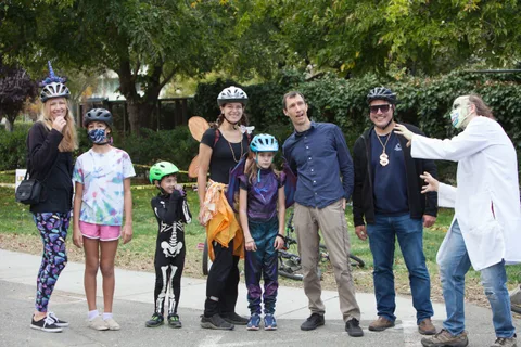 A family group in costume, including a skeleton and a doctor, shares a candid moment.