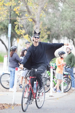 A man in a black bat costume spreads his arms wide while riding through the group.