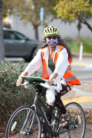 A rider in an orange safety vest costume and mask pedals down the street.