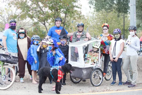 A large costumed group poses with a cargo bike and a dog.