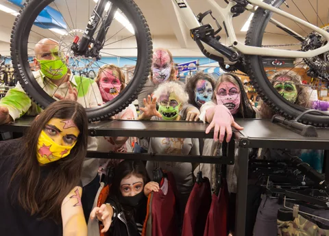 A cluster of zombie-painted riders gathers together with a bike overhead.