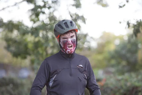 A rider in zombie face paint and a helmet looks toward the camera in close up.