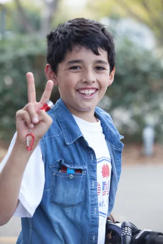 A boy in a denim jacket gives a peace sign and grins at the camera.