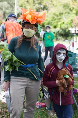 Two women in costume, one with an orange leaf headdress, stand together in the park.