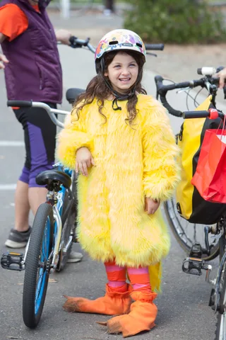 A girl in a fuzzy yellow chick costume smiles while riding her bike.