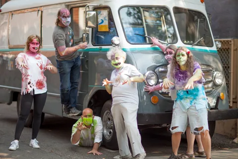 A costumed group poses in front of a vintage van.