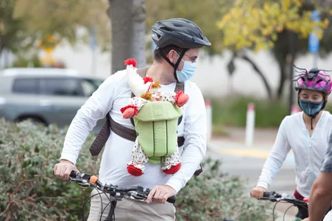 A masked rider carries a stuffed animal decoration on her back while riding.