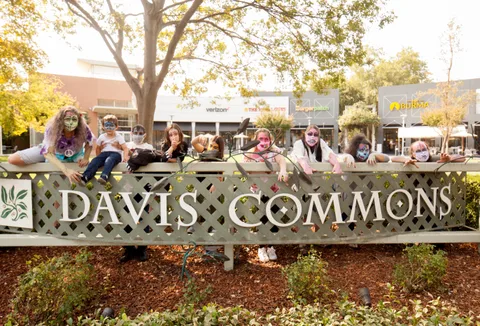 A row of zombie-painted riders leans over the Davis Commons sign in warm afternoon light.