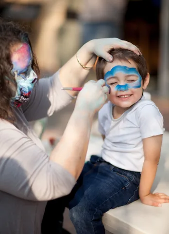A volunteer carefully paints a blue design on a young boy's face.