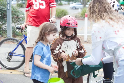A man in a football jersey stands with two children in animal costumes and bikes.