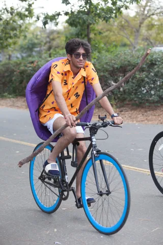 A rider in an orange costume with sunglasses looks away from the camera on a bike path.
