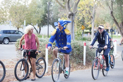 Two riders in costume pedal along the path at a distance from each other.