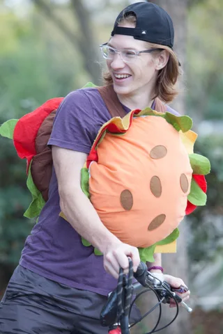 A rider in a giant strawberry costume holds the handlebars, face out of frame.
