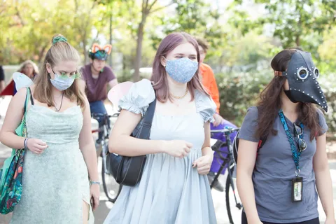 Two women in flowing grey and blue dresses walk their bikes together.
