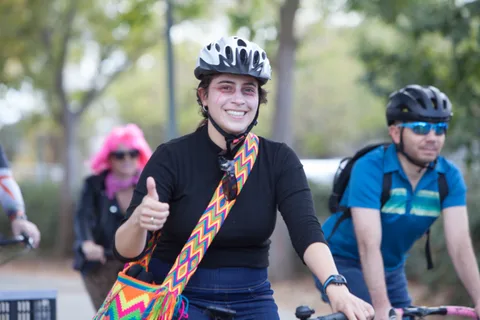 A woman with a colorful crossbody bag smiles and gives a thumbs up.