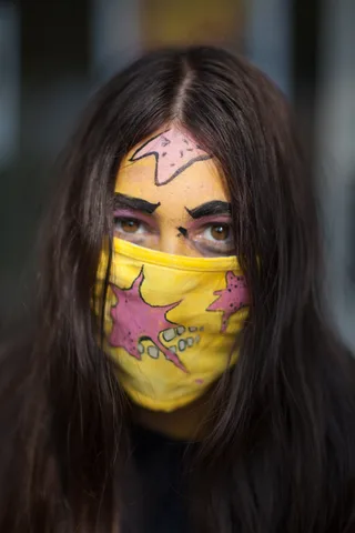 A close portrait shows dramatic pink and blue face paint around watchful eyes.