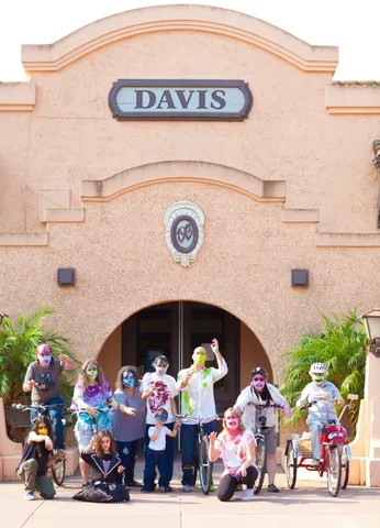 A large group of zombie-painted riders gathers outside a downtown archway.