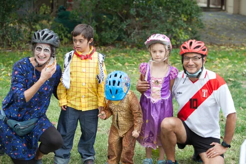 A father in a soccer jersey kneels with four costumed children for a group photo.