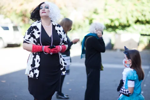 A woman in a cow-print jacket walks past with another costumed figure behind her.