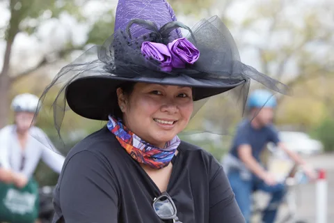 A woman in an elaborate purple witch hat with black tulle smiles warmly at the camera.
