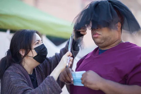 A woman playfully adjusts a mask over a man's face.