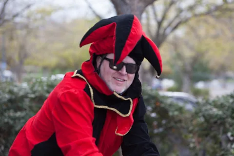A man in a red and black jester devil costume poses in sunglasses.