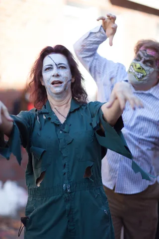 A woman in white zombie face paint gestures dramatically with another costumed figure behind her.
