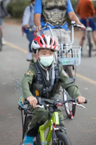 A masked child rides a bike with a costumed adult following close behind.