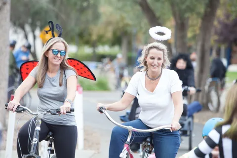 Two women ride together, one wearing small ladybug wings and the other a halo.
