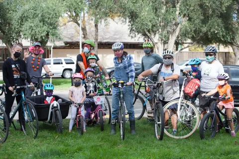 Several families with bikes gather on the grass, some wearing masks.