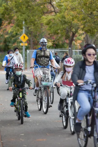 A group of masked kids rides bikes together in costume down the path.