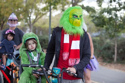 A child in a green hooded costume sits with an adult wearing a Grinch mask and scarf.