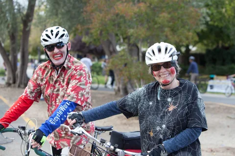 Two riders in bloody zombie doctor costumes smile together while holding their bikes.