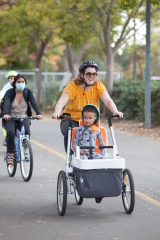 Two riders, one towing a child trailer, ride away from the camera.